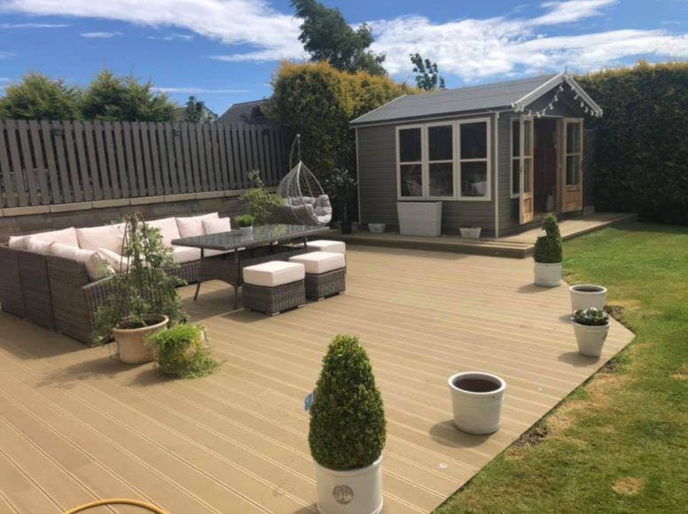 Large deck with garden furniture and planters leading to a summer house