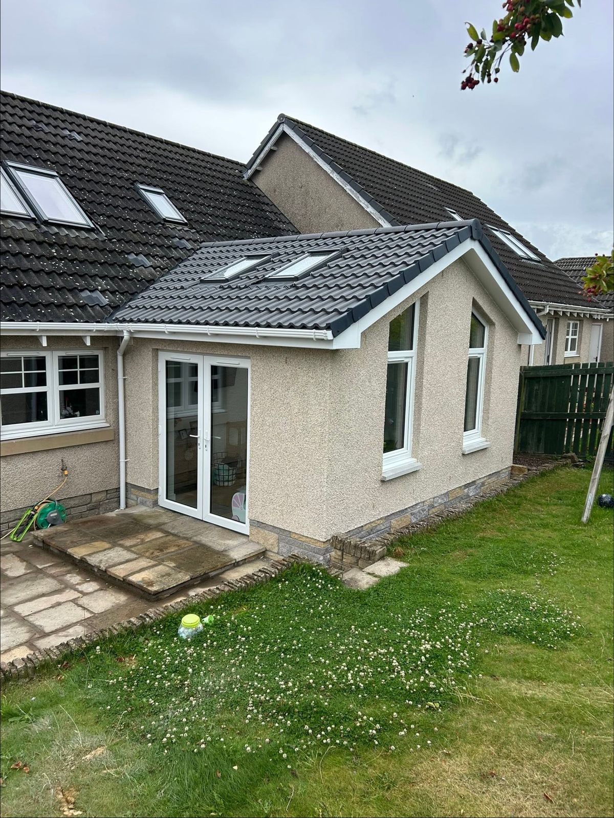 Rendered single storey extension with a tiled gable roof, roof windows and French doors onto a lawn
