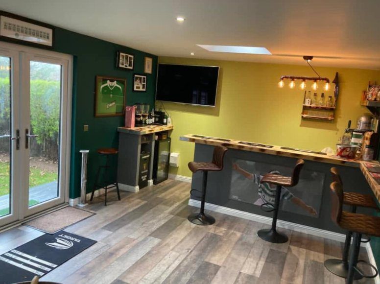 Garden room fitted out as a bar, with French doors, bar stools and a wood effect floor