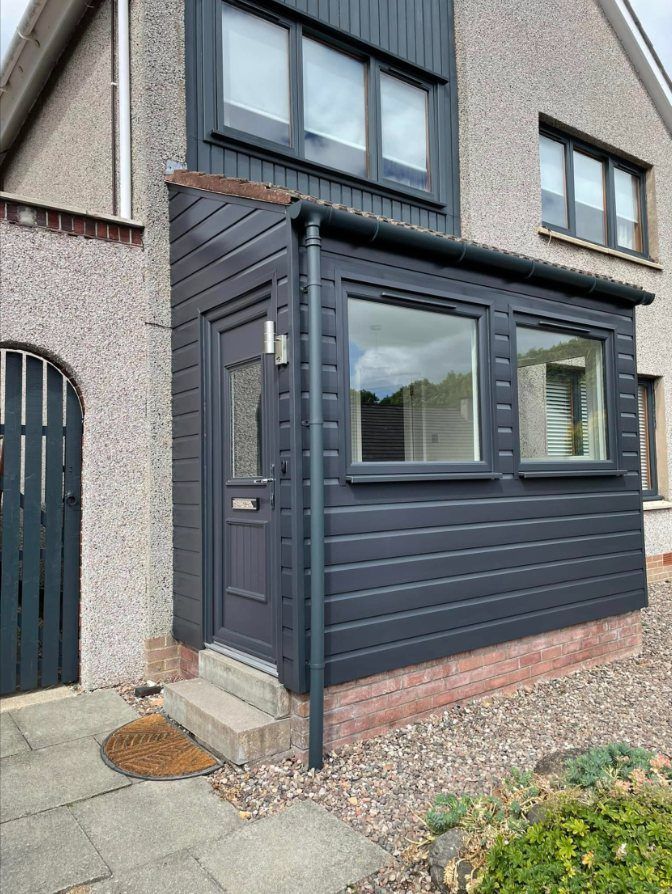 New porch clad in dark grey boards with a front door and two windows, on the same house